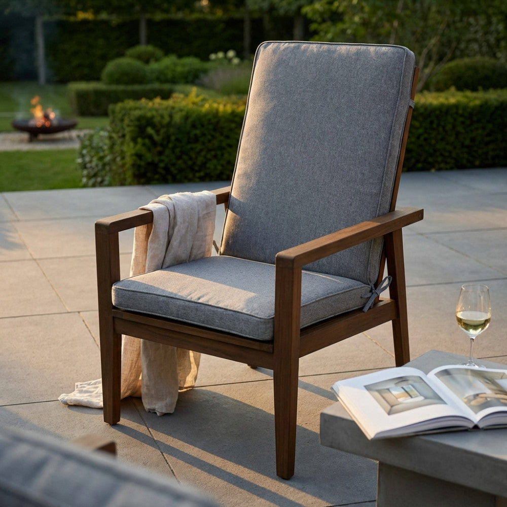 Cuscino Real Medio grigio chiaro posizionato su una poltrona in legno da esterni, illuminato dalla luce del tramonto in un giardino curato.