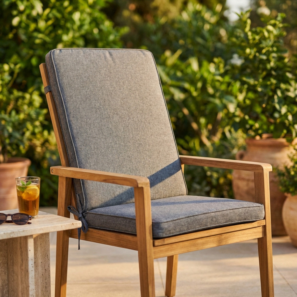 Cuscino Real Medio grigio scuro posizionato su una sedia in legno di teak in un giardino soleggiato.