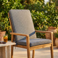 Cuscino Real Medio grigio scuro posizionato su una sedia in legno di teak in un giardino soleggiato.