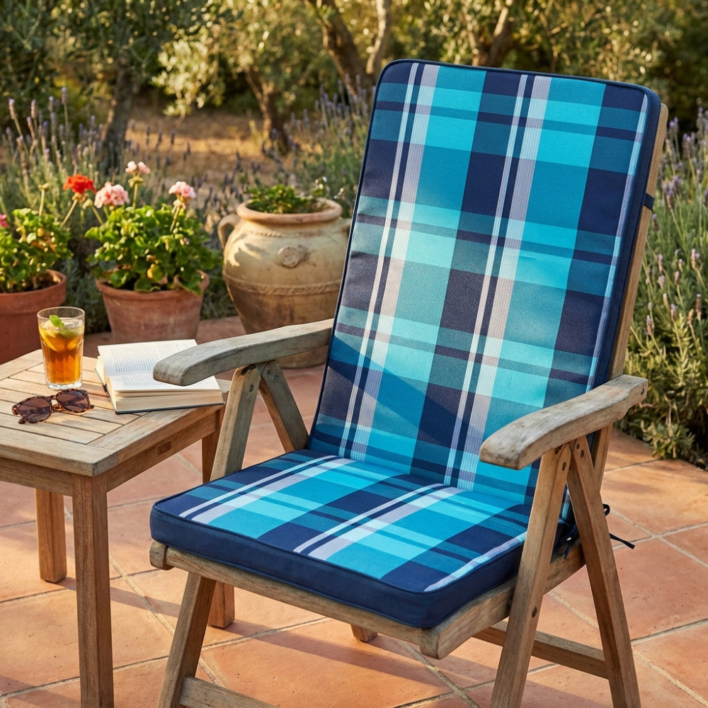 Cuscino Real Medio Quadri Blu posizionato su una sedia pieghevole in legno in un giardino rigoglioso.