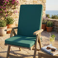 Cuscino Real Medio verde scuro posizionato su una sedia in legno da esterni, in un patio soleggiato con vista mare.
