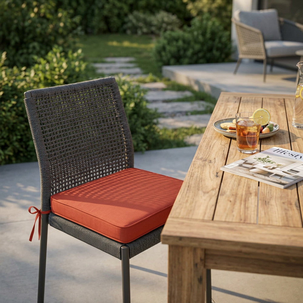 Cuscino arancione adagiato su una poltroncina da giardino con schienale in corda intrecciata e struttura scura.