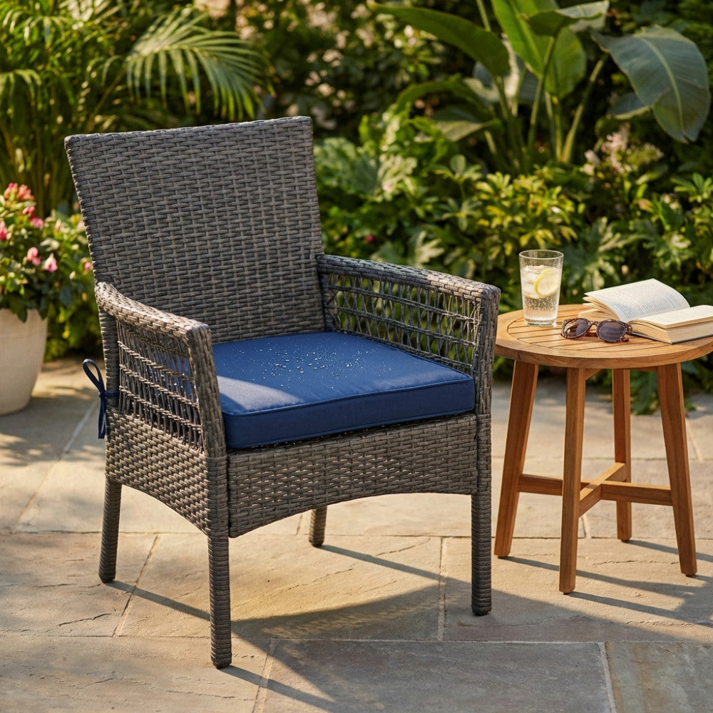 Cuscino seduta Real blu scuro su una poltroncina in midollino sintetico, con gocce d'acqua che ne evidenziano la superficie idrorepellente.