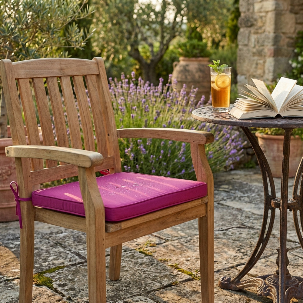 Cuscino Real Seduta color magenta posizionato su una sedia in legno da esterni, con gocce d'acqua sulla superficie idrorepellente, in un giardino soleggiato.