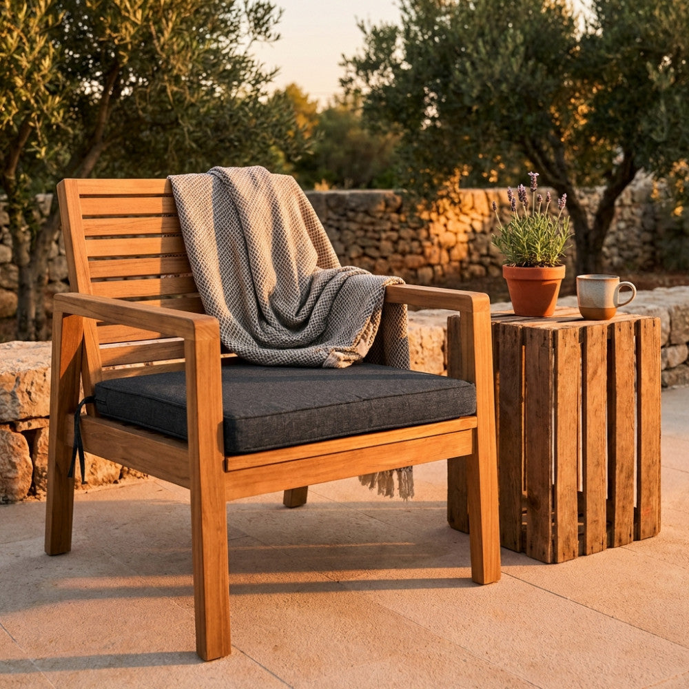 Sedia in legno con cuscino grigio scuro e coperta testurizzata, in un giardino rustico al tramonto.