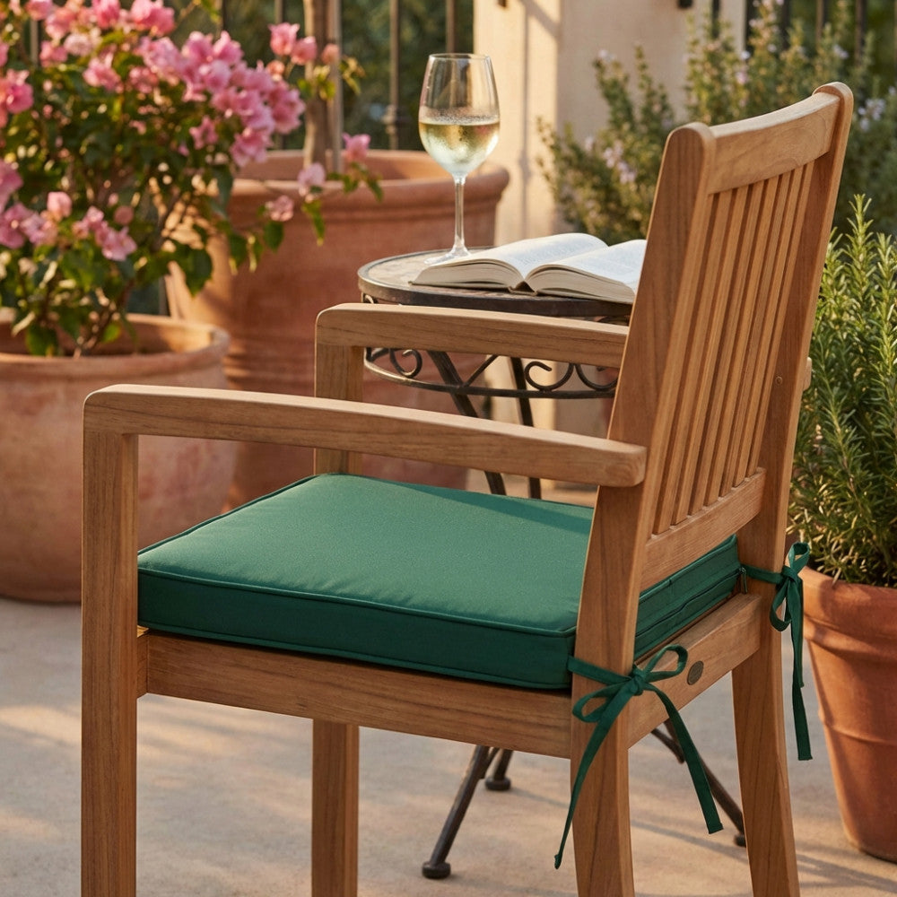 Dettaglio del cuscino verde scuro su una sedia in legno, in un elegante patio con fiori e un bicchiere di vino.