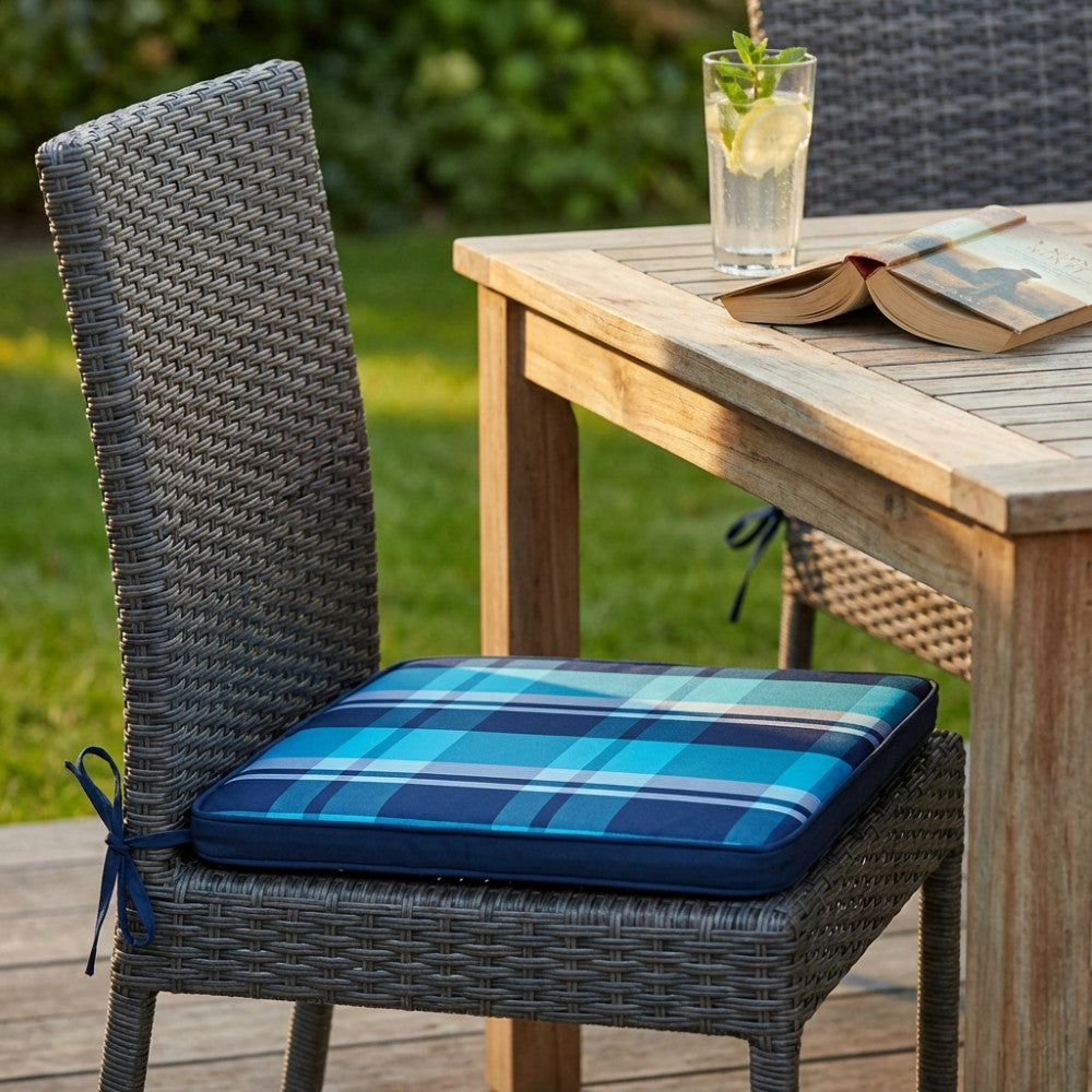 Dettaglio del cuscino moderno blu azzurro su sedia da esterni, accanto a un tavolo in legno con libro e bibita.