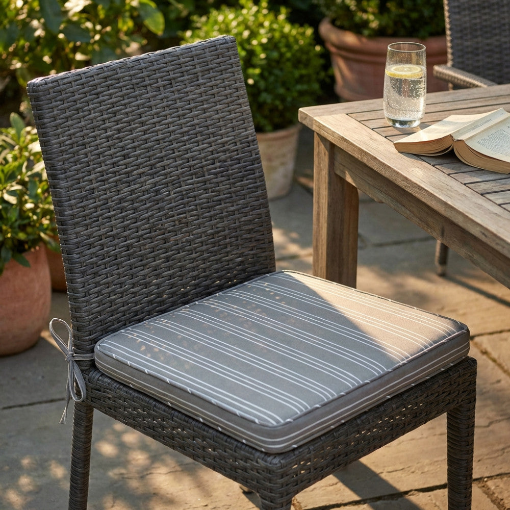 Cuscino seduta a righe tortora posizionato su una sedia in rattan intrecciato scuro in un giardino.