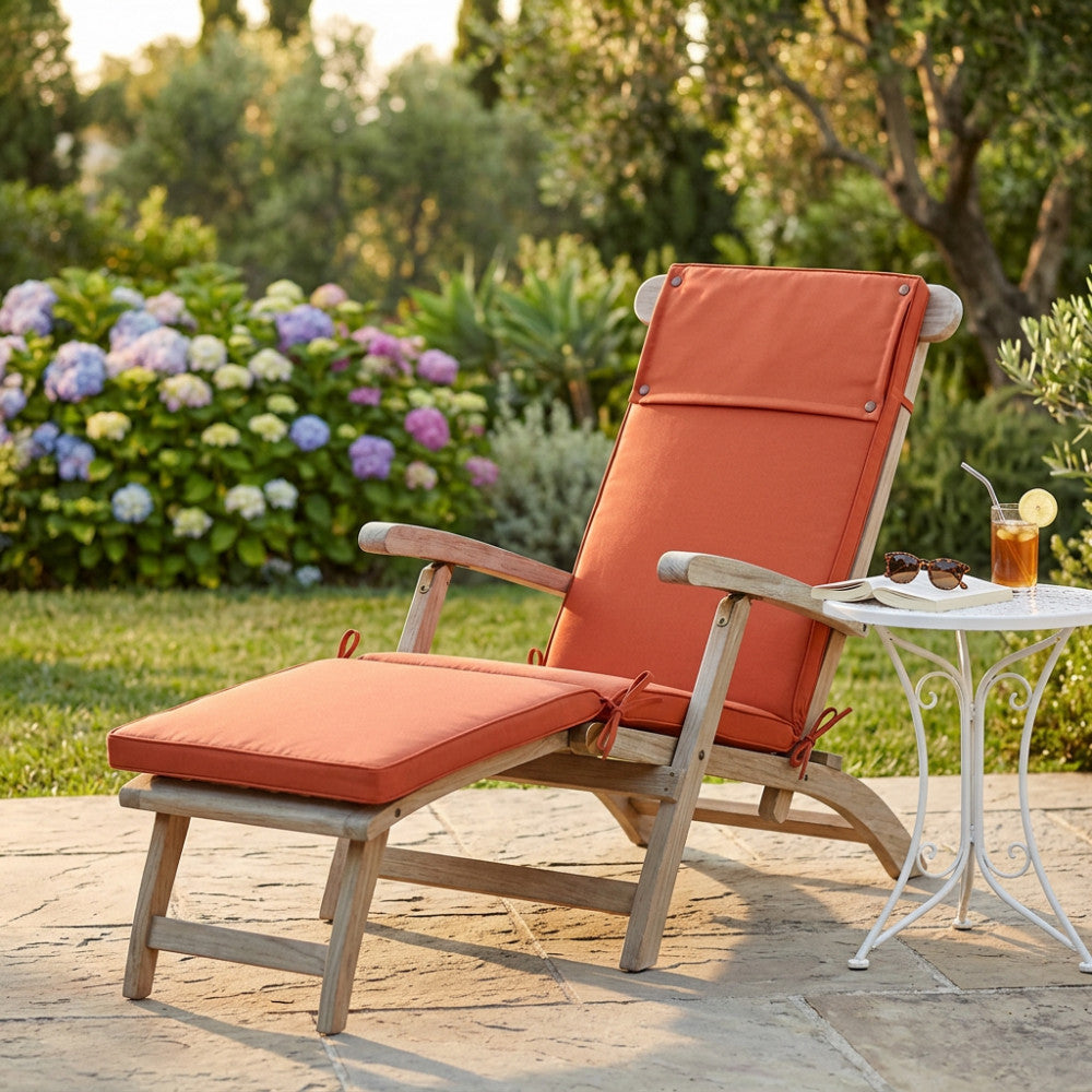 Cuscino Real Steamer arancione posizionato su una sdraio in legno in un rigoglioso giardino.