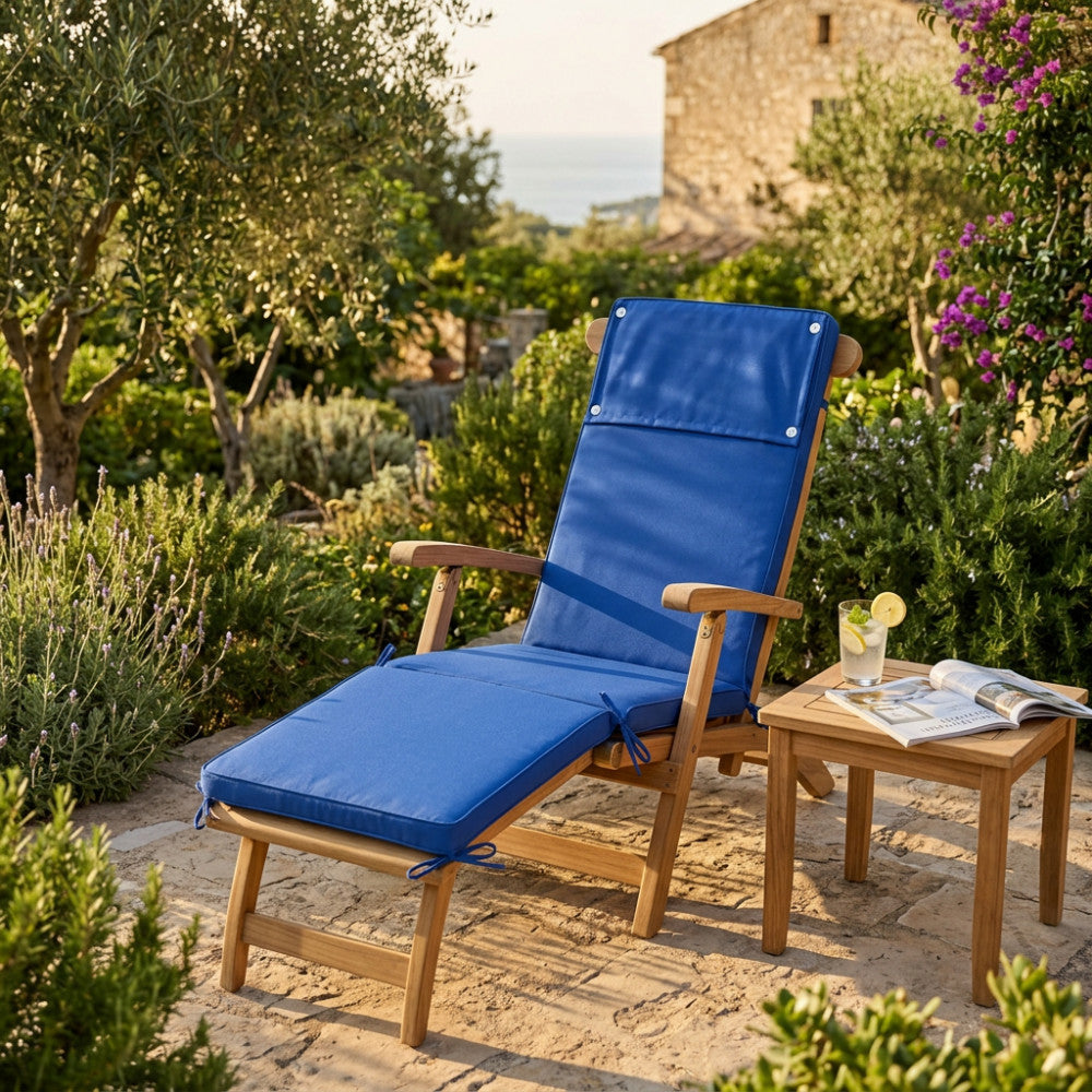Cuscino steamer blu scuro posizionato su una sedia a sdraio in legno in un rigoglioso giardino mediterraneo.