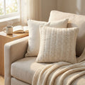 Cuscino Renaud in lana e cotone bianco posizionato su una poltrona beige, illuminato dalla luce naturale.