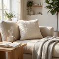 Cuscino Théodore in lana bianca posizionato su un divano beige illuminato dalla luce naturale.