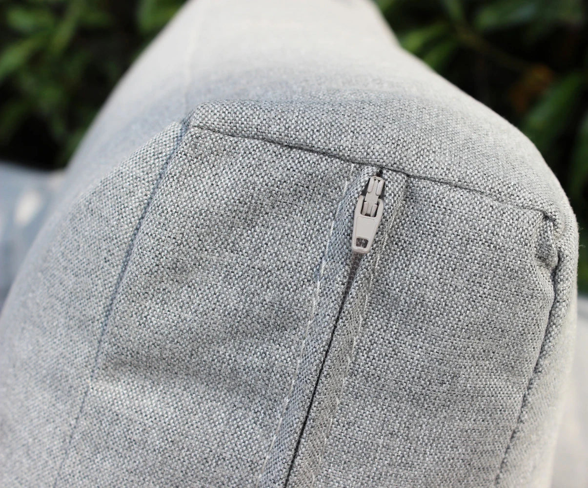 Dettaglio cuscino sfoderabile del Set salotto da esterno Madeira 2P in alluminio verniciato antracite con cuscini grigi, composto da divano a due posti, due poltrone e un tavolino, ambientato in un patio con ghiaia bianca e parete in pietra.