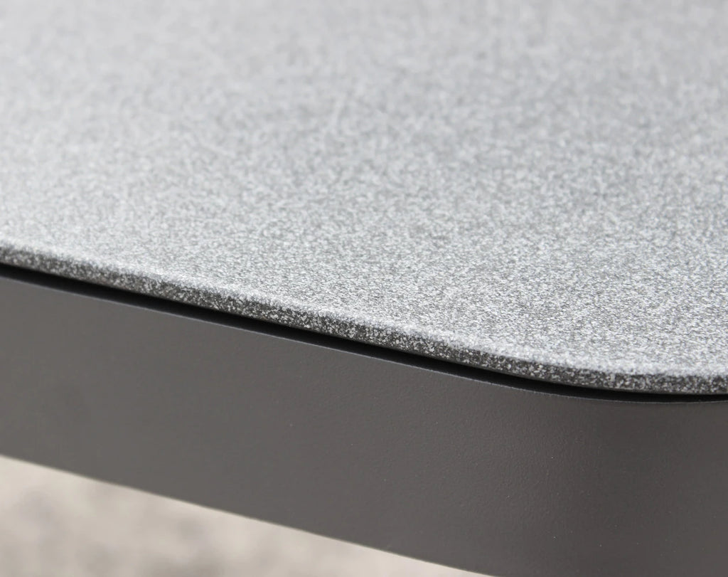 Dettaglio dei cuscini del Set salotto da esterno Madeira 2P in alluminio verniciato antracite con cuscini grigi, composto da divano a due posti, due poltrone e un tavolino, ambientato in un patio con ghiaia bianca e parete in pietra