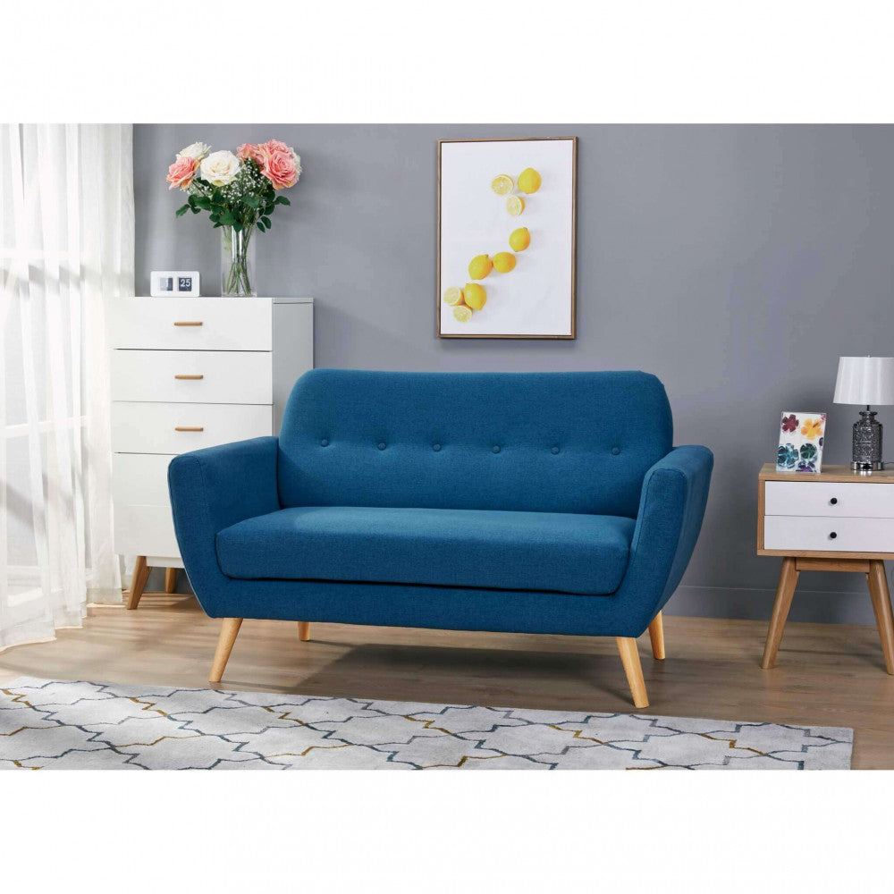 Divano moderno blu ambientato in un salotto con pareti grigie, cassettiera bianca e stampe decorative a parete.