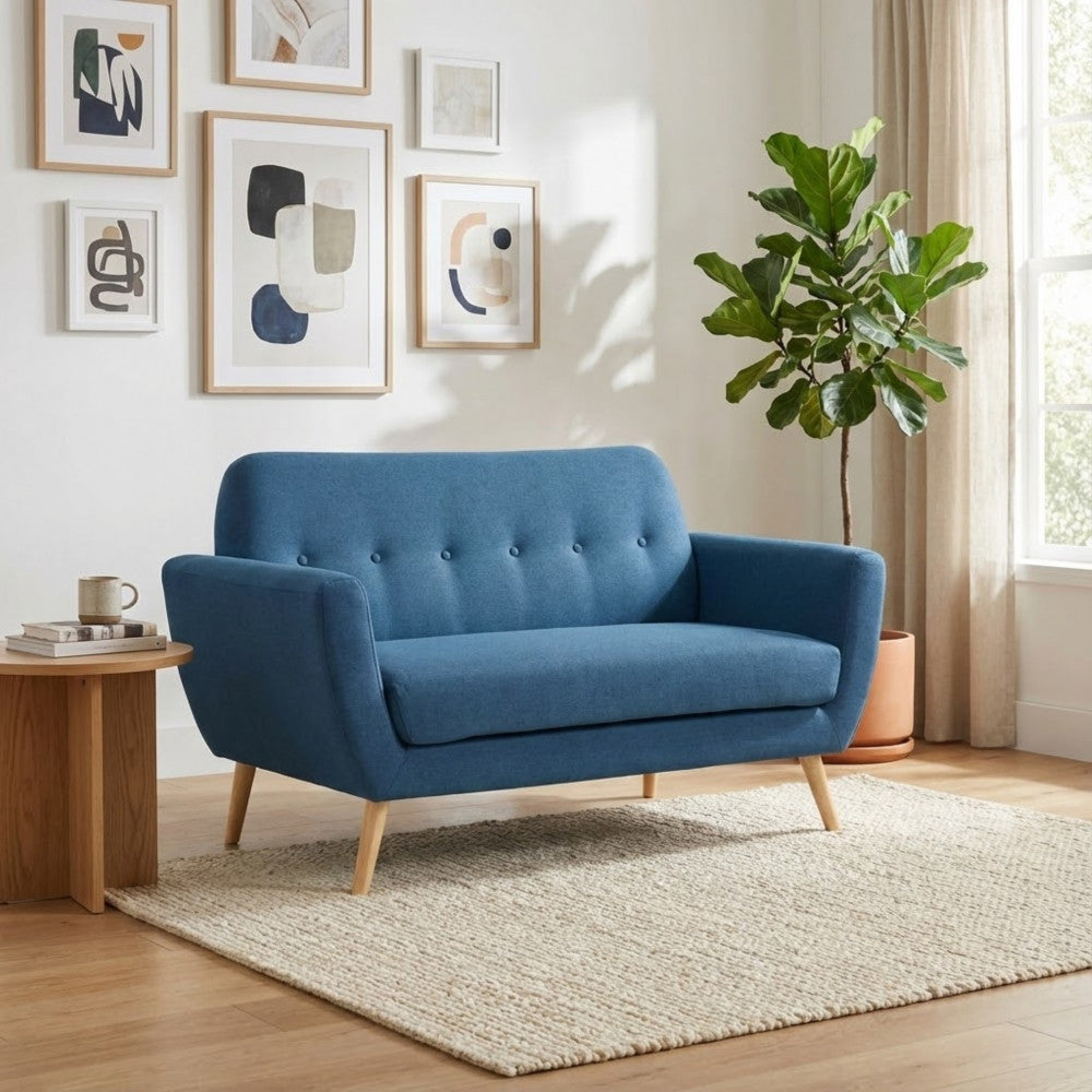 Divano blu di design posizionato in una stanza luminosa con gallery wall, pianta ornamentale e tavolino in legno.