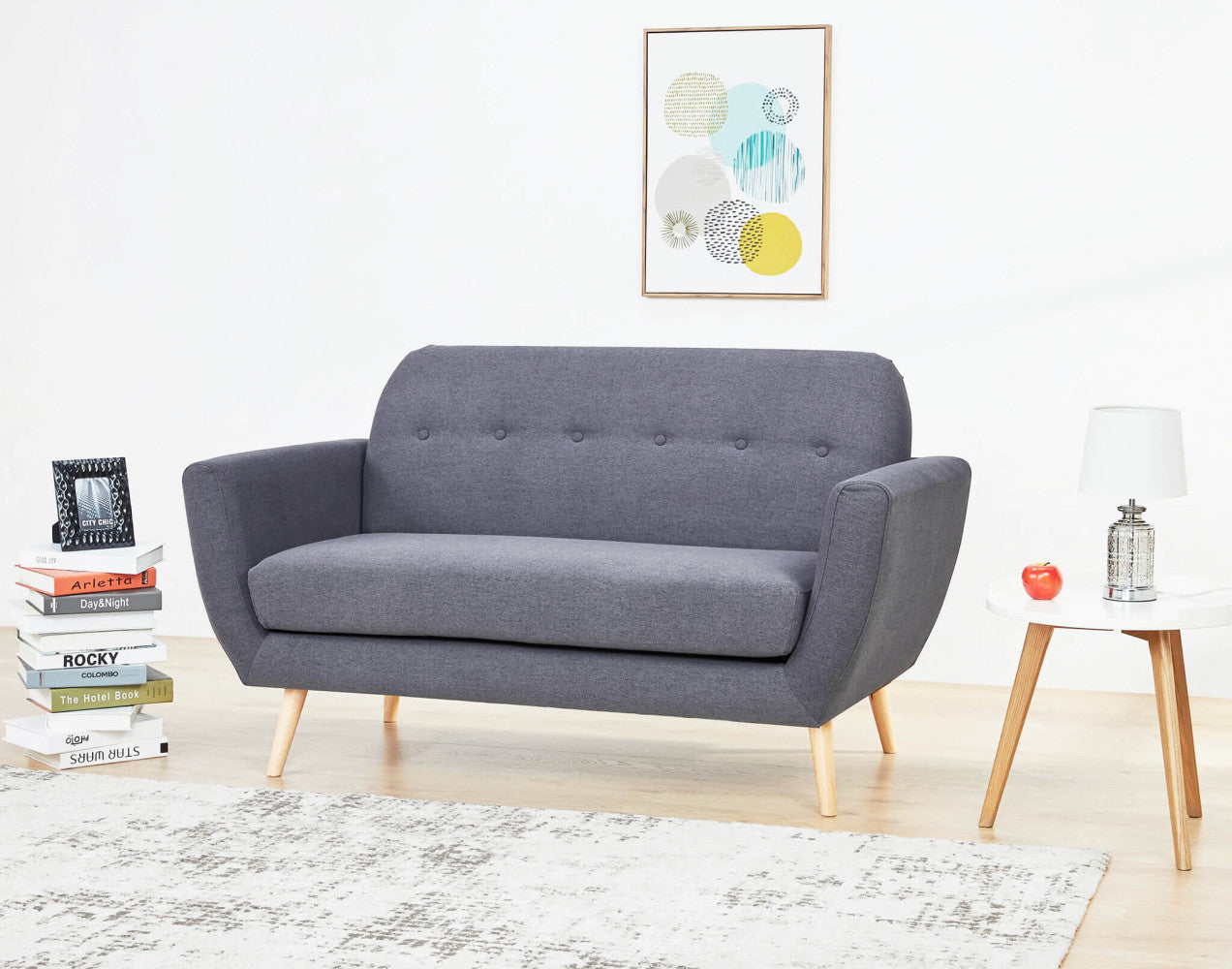 Ambientazione contemporanea con il divano 2 posti Burton grigio scuro, affiancato da una pila di libri di design e un tavolino bianco.