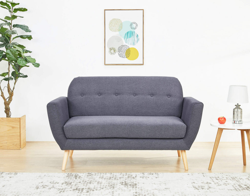 Inquadratura frontale del divano Burton in un contesto minimalista, decorato con una pianta d'appartamento e stampe geometriche a parete.