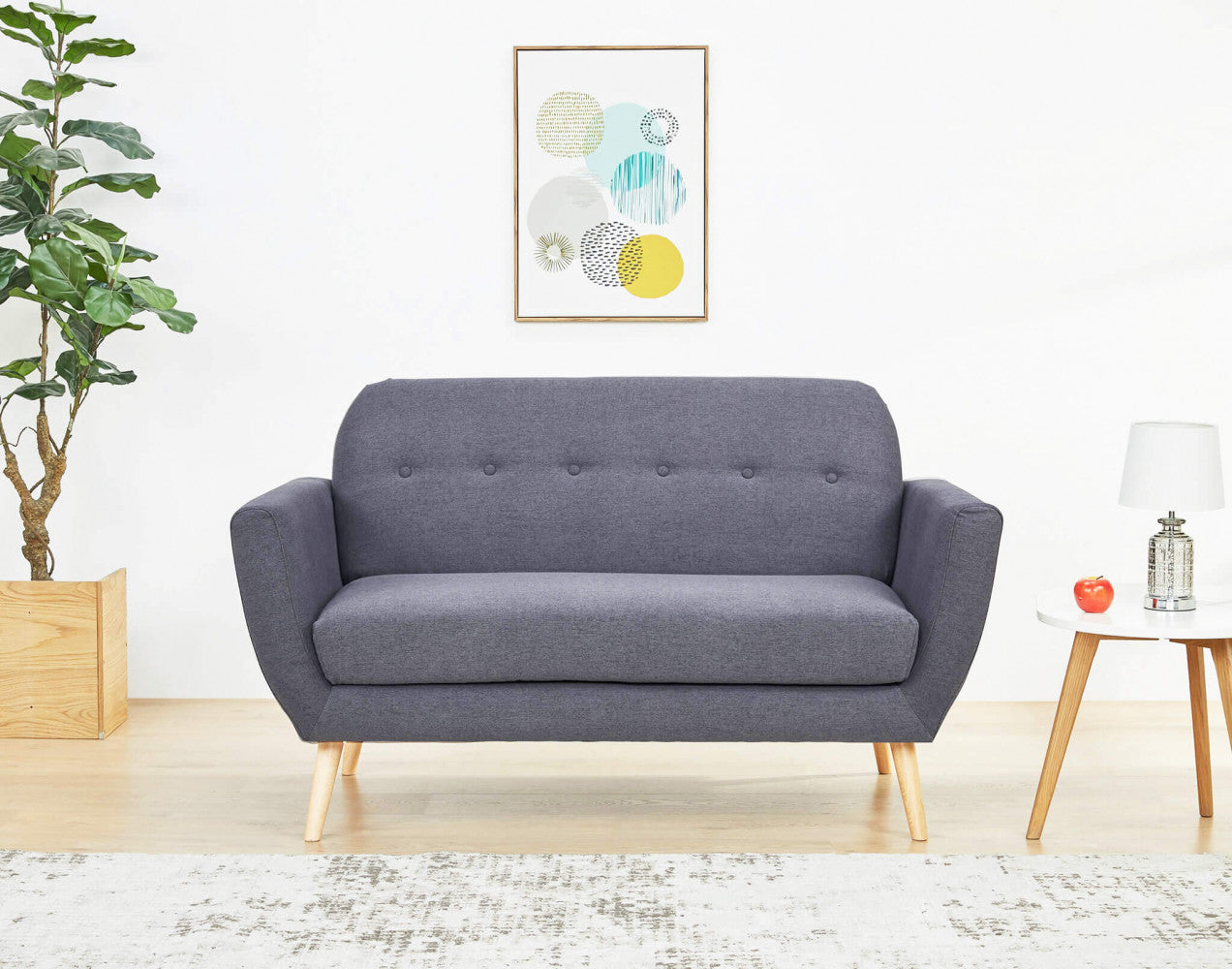 Inquadratura frontale del divano Burton in un contesto minimalista, decorato con una pianta d'appartamento e stampe geometriche a parete.
