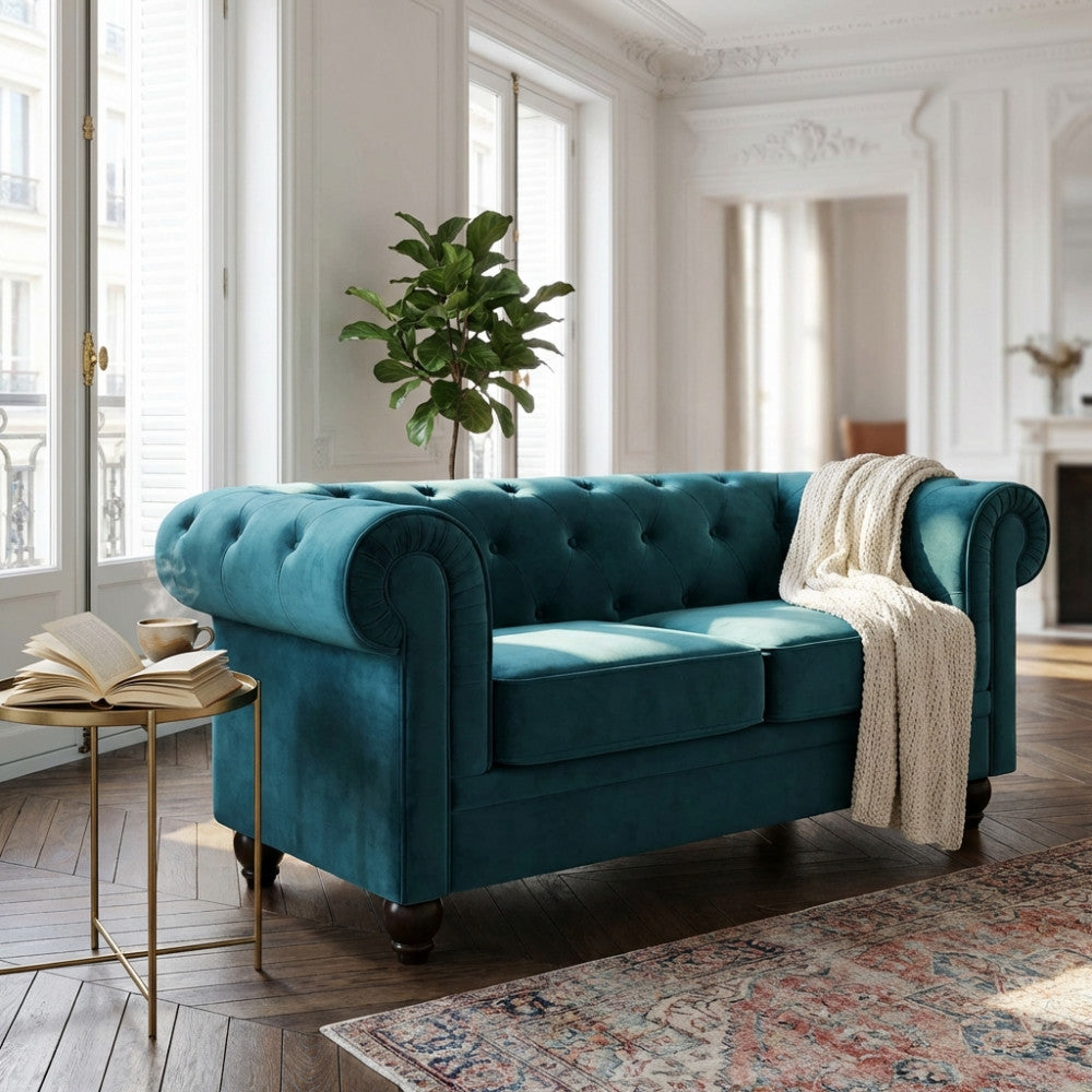 Divano 2 posti Chesterfield in velluto blu ambientato in un luminoso salotto con pianta decorativa.