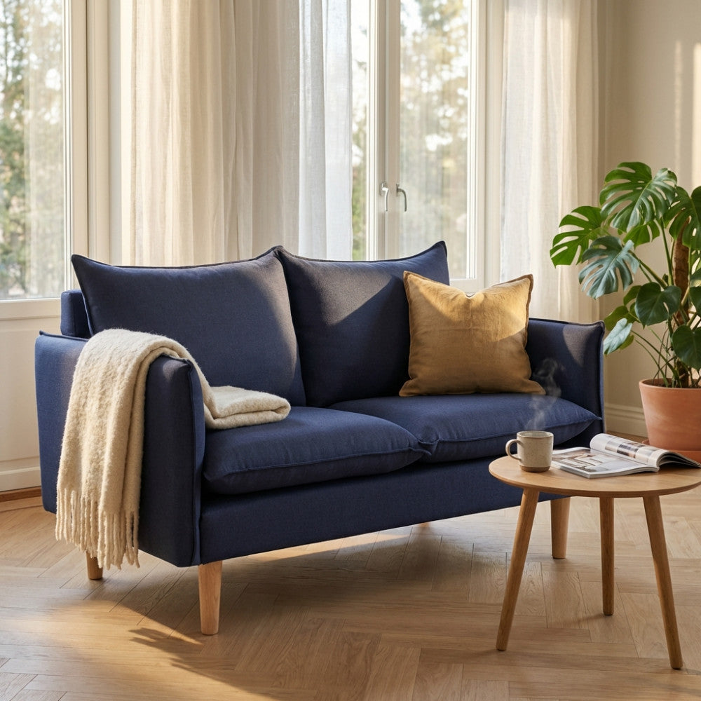Dettaglio del divano 2 posti Florin blu illuminato dalla luce naturale, con cuscino decorativo senape e coperta in maglia.