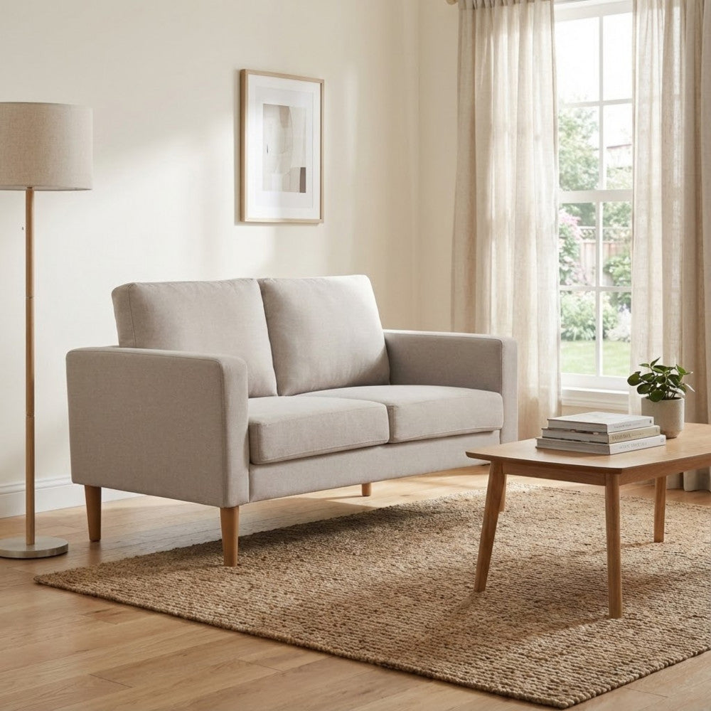 Divano 2 posti Ramsey beige inserito in un ambiente caldo con tappeto in iuta e tavolino in legno.