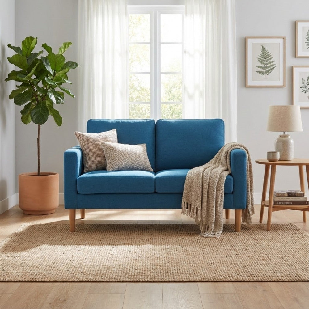 Salotto elegante con il divano 2 posti Ramsey blu, tappeto in iuta, tavolino laterale e grande finestra luminosa.