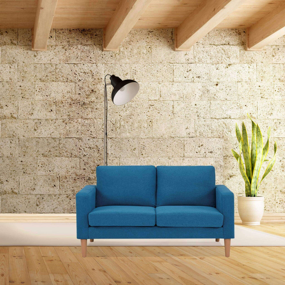 Divano 2 posti Ramsey blu inserito in un ambiente dal design rustico-chic con parete in pietra e soffitto in legno.