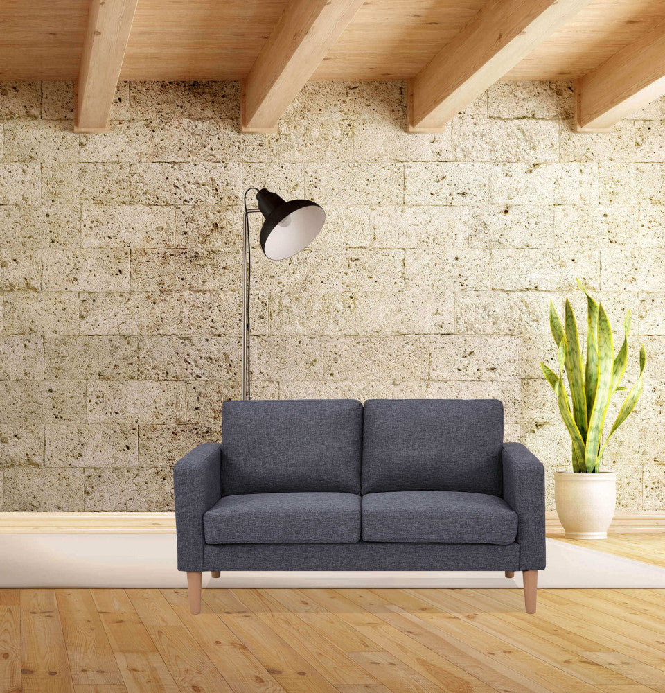 Divano a due posti Ramsey inserito in un loft con pareti in pietra chiara, soffitto in legno e una lampada da terra nera.