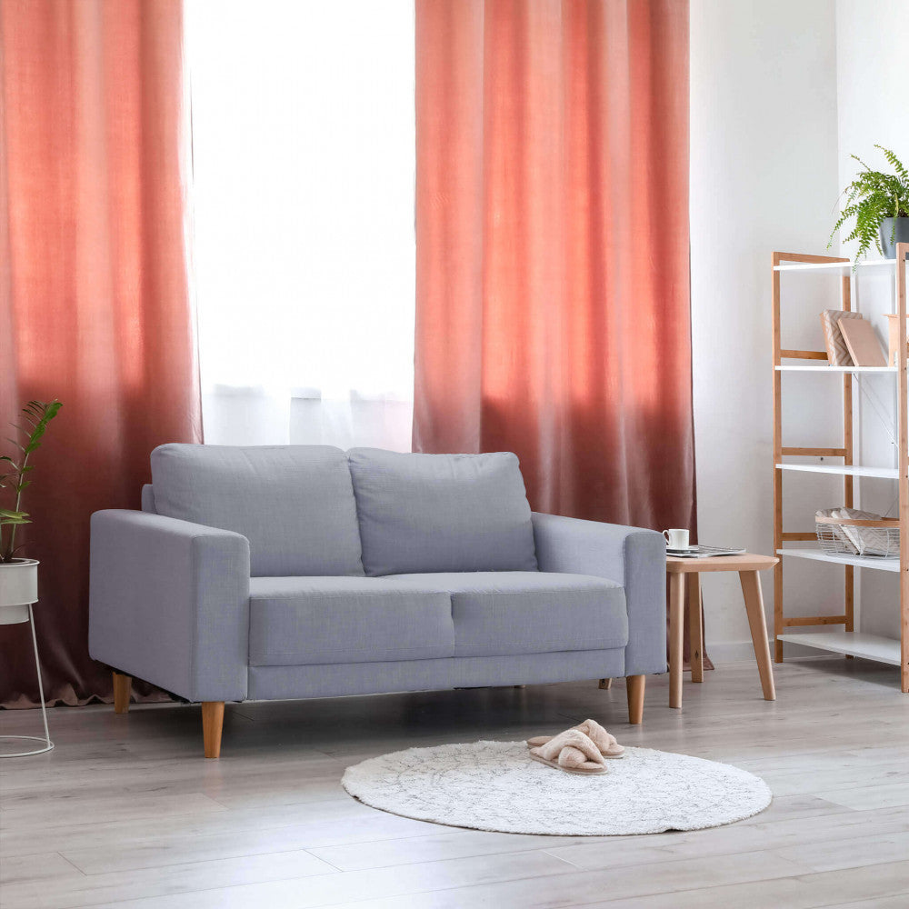 Divano Ramsey inserito in un salotto moderno con tende color ruggine e libreria in legno chiaro.