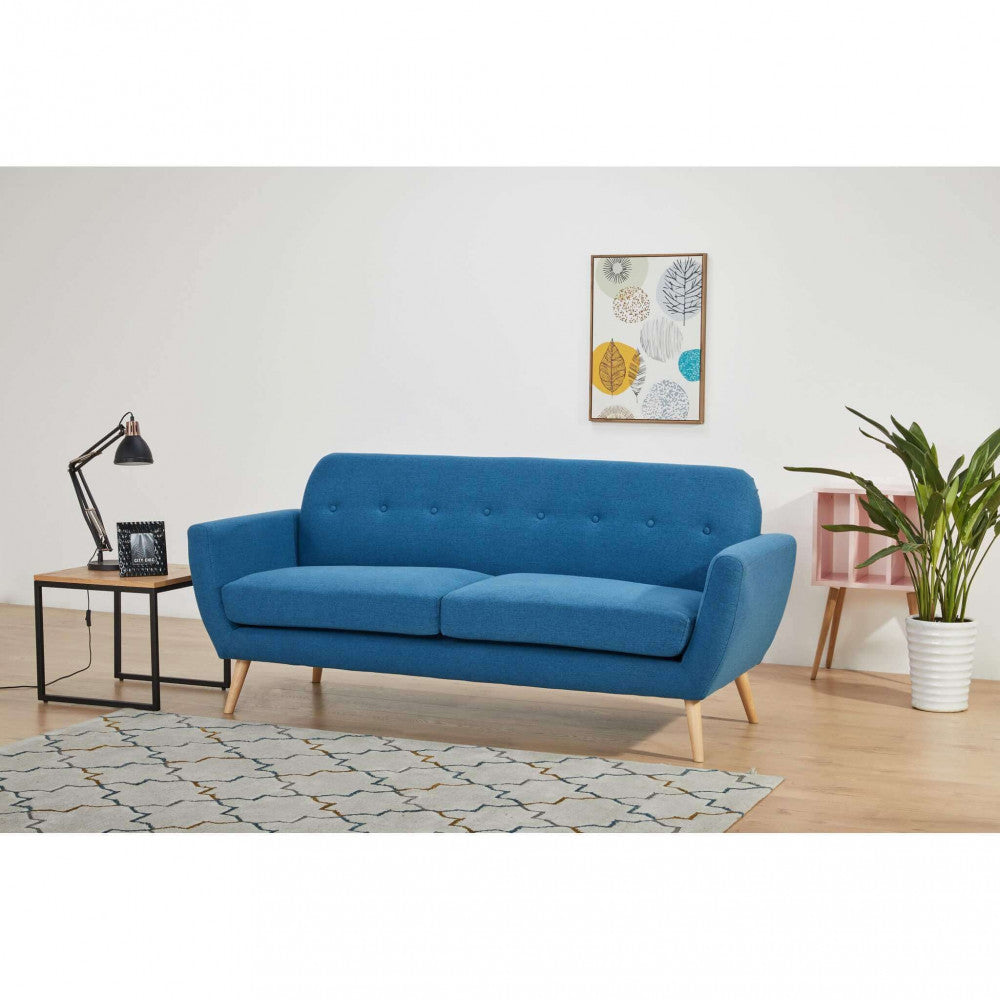 Divano a tre posti Burton blu posizionato in un ambiente minimalista con tappeto geometrico e decorazioni a parete.