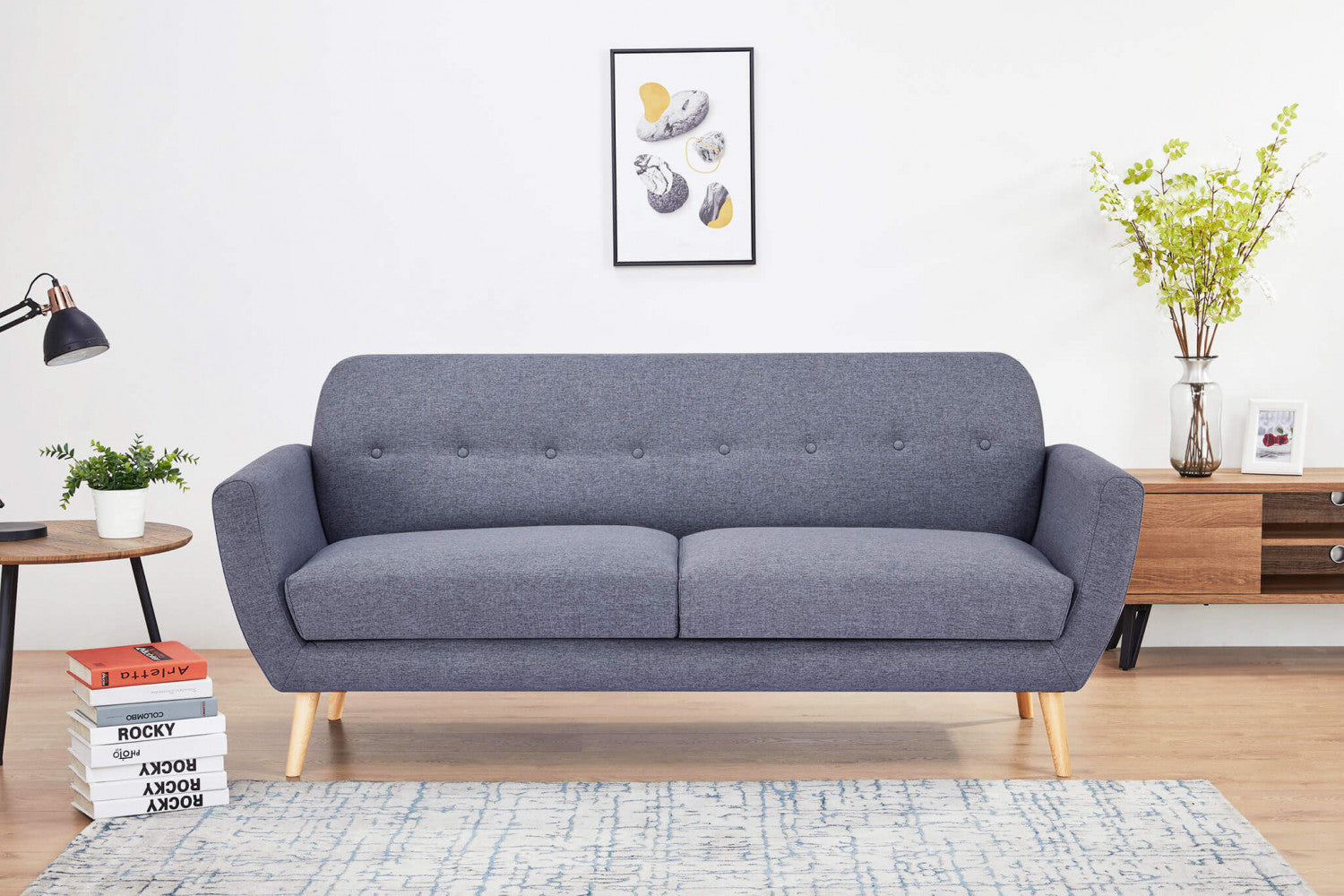 Divano Burton grigio scuro ambientato in un living moderno con tavolino in legno, libri e tappeto chiaro.