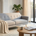 Divano 3 posti Burton in tessuto grigio chiaro ambientato in un living luminoso con tavolino in legno e pianta decorativa.