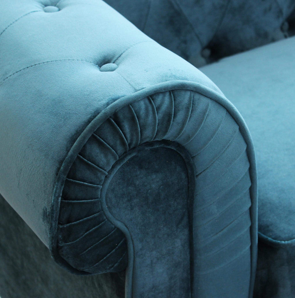 Dettaglio ravvicinato del bracciolo arrotondato del divano Chesterfield in velluto blu con pieghe sartoriali.