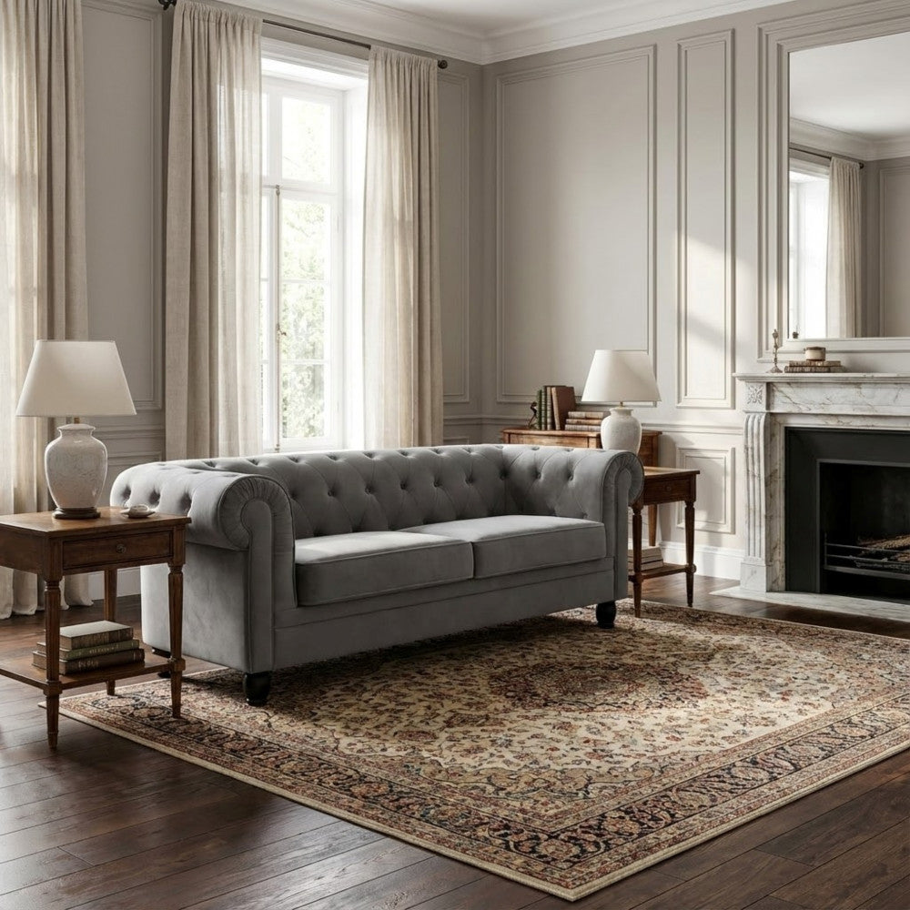 Divano Chesterfield in velluto grigio inserito in un salotto classico contemporaneo con tappeto persiano e camino in marmo.