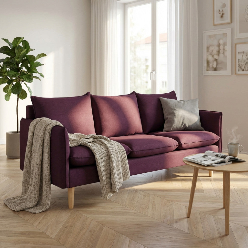 Divano 3 posti Florin in tessuto viola ambientato in un luminoso soggiorno moderno con pavimento in parquet.