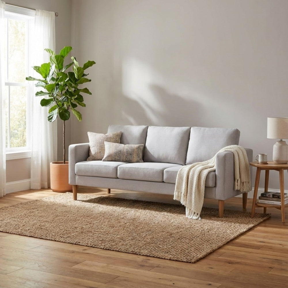 Soggiorno completo con il divano 3 posti Ramsey beige, tappeto materico e pianta ornamentale per un'atmosfera rilassante.