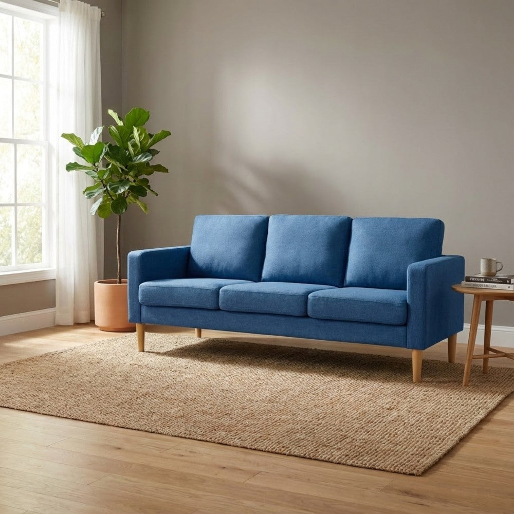 Divano Ramsey blu inserito in un salotto dal design nordico con tappeto in iuta grezza e tavolino laterale in legno.