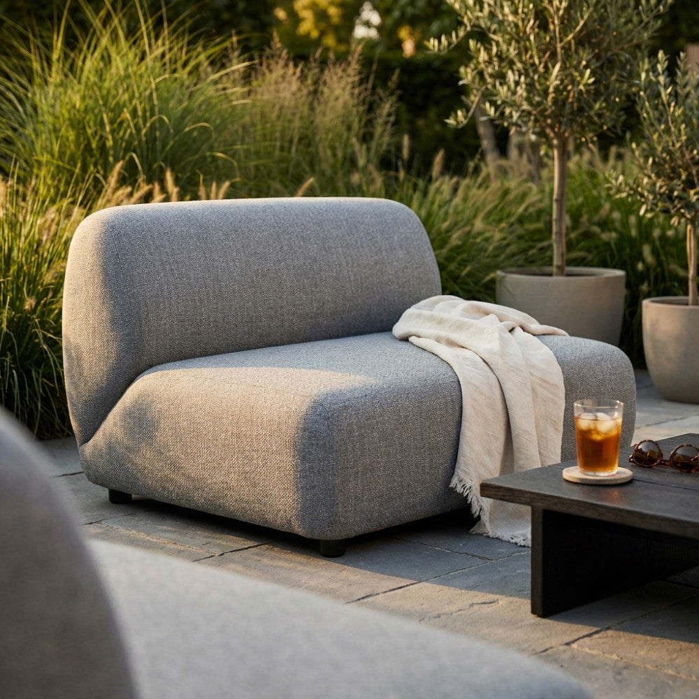 Modulo centrale divano Vancouver in poliestere grigio, ambientato all'aperto con coperta decorativa e tavolino.