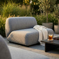 Modulo centrale divano Vancouver in poliestere grigio, ambientato all'aperto con coperta decorativa e tavolino.