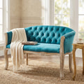Divano 2 posti Coleman in velluto blu e legno, ambientato in un salotto classico con plaid chiaro.