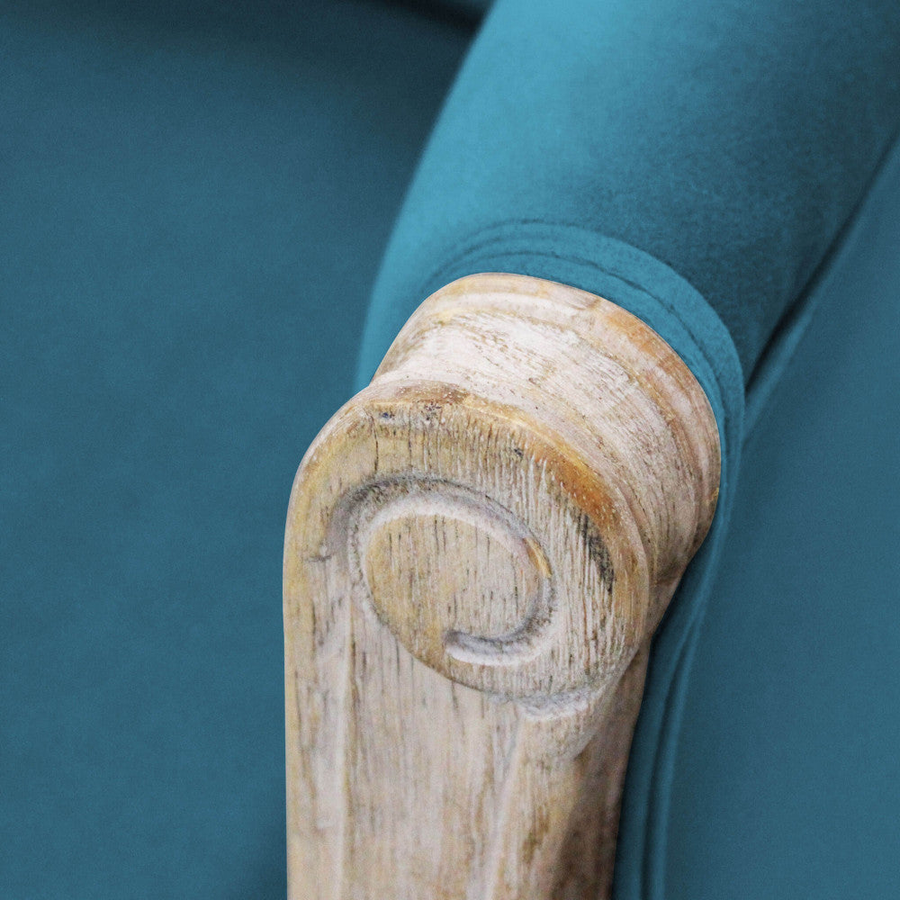 Primo piano del bracciolo in legno lavorato a mano, che contrasta con la morbidezza del velluto blu.