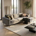 Divano con chaise longue Gregory in tessuto grigio, ambientato in un living luminoso con tappeto chiaro e un piccolo ulivo decorativo.
