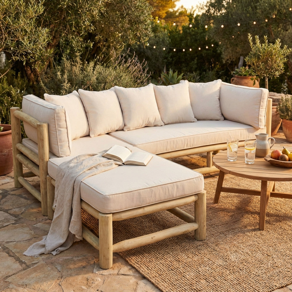 Divano con chaise longue Martinez in teak con cuscini tortora, ambientato in un giardino mediterraneo al tramonto.