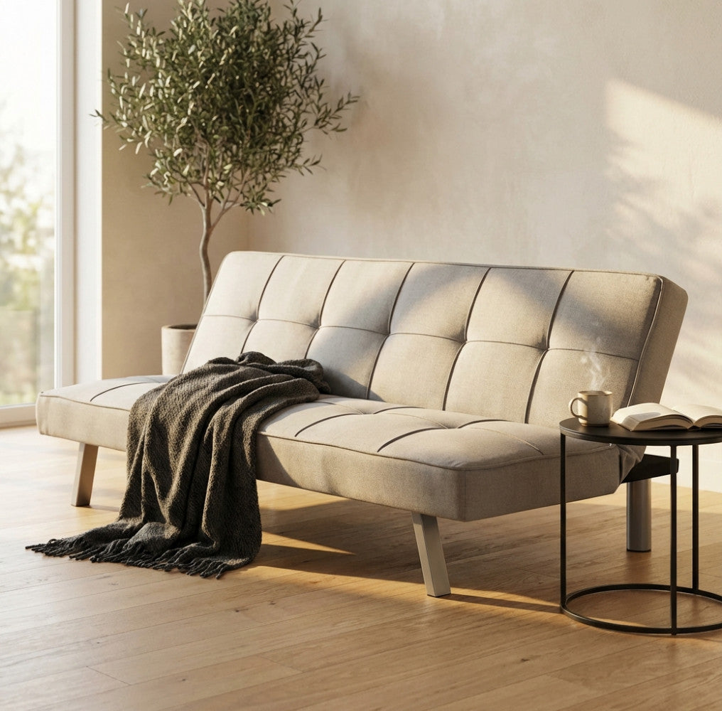 Divano letto Aaron a tre posti in tessuto grigio chiaro, ambientato in un luminoso soggiorno moderno con luce naturale e una pianta di ulivo.