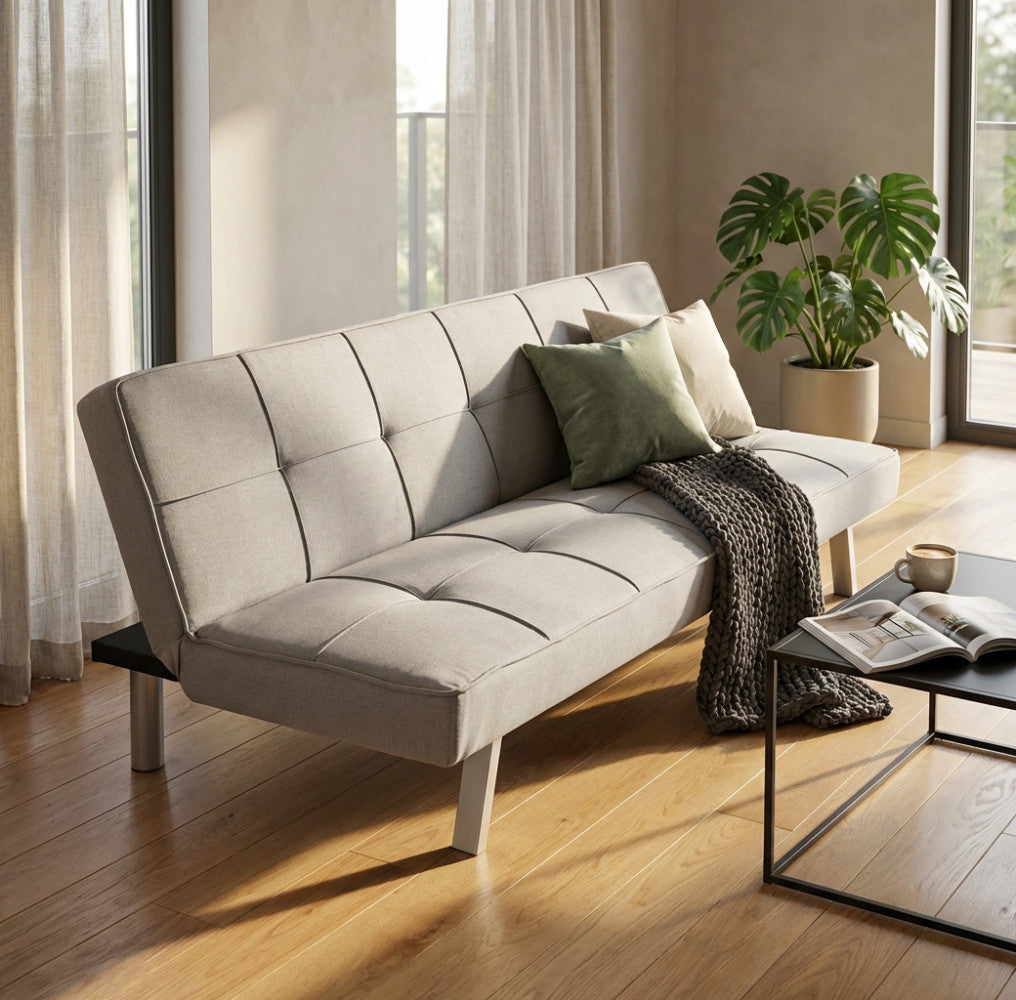 Vista angolare del divano letto Aaron grigio chiaro, decorato con cuscini verdi e beige, affiancato da un tavolino nero in un salotto elegante.