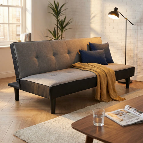 Divano letto Alvin in tessuto grigio ambientato in un living moderno con illuminazione calda e pavimento in parquet.