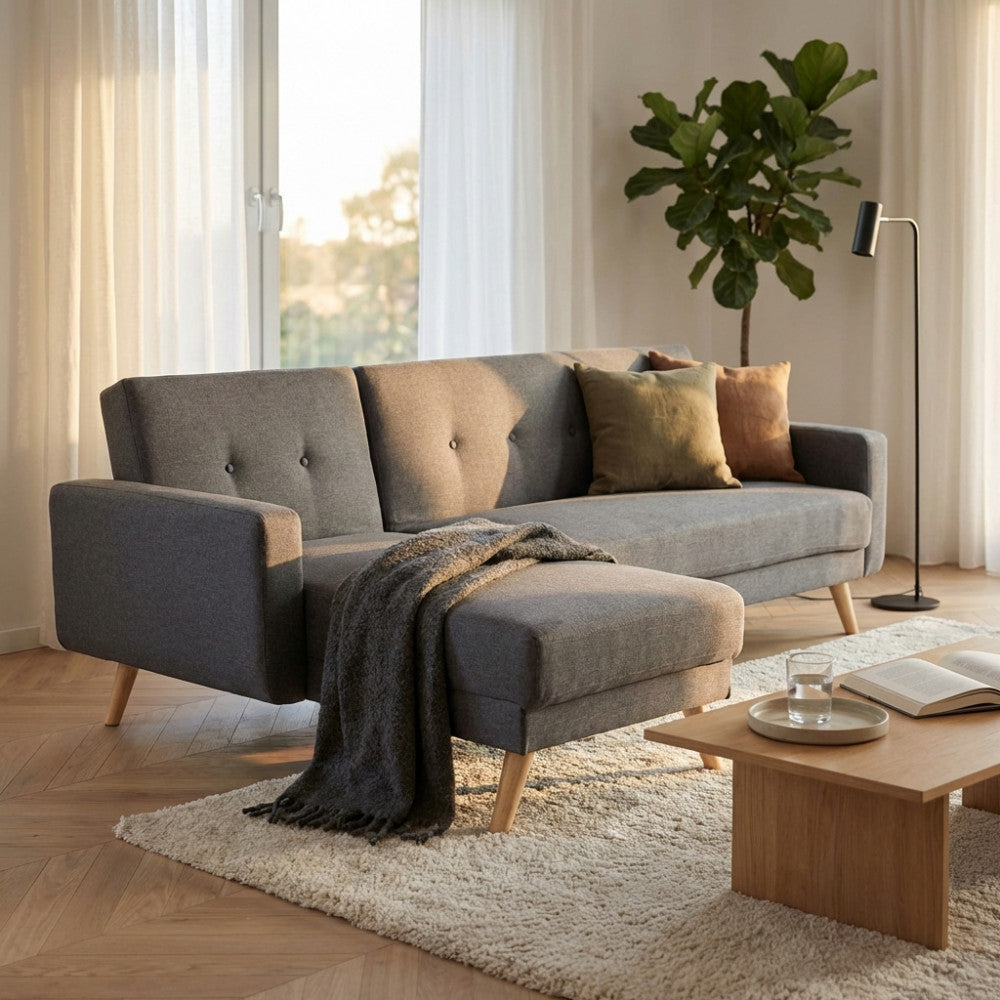 Divano letto Arthur a 4 posti in tessuto grigio scuro, ambientato in un luminoso soggiorno moderno con luce naturale.