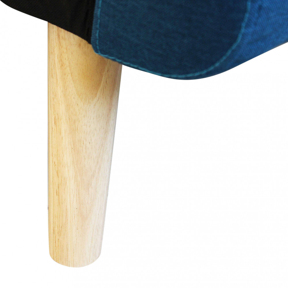 Dettaglio ravvicinato del piedino affusolato in legno massello e delle cuciture sartoriali sul tessuto blu melange del divano.