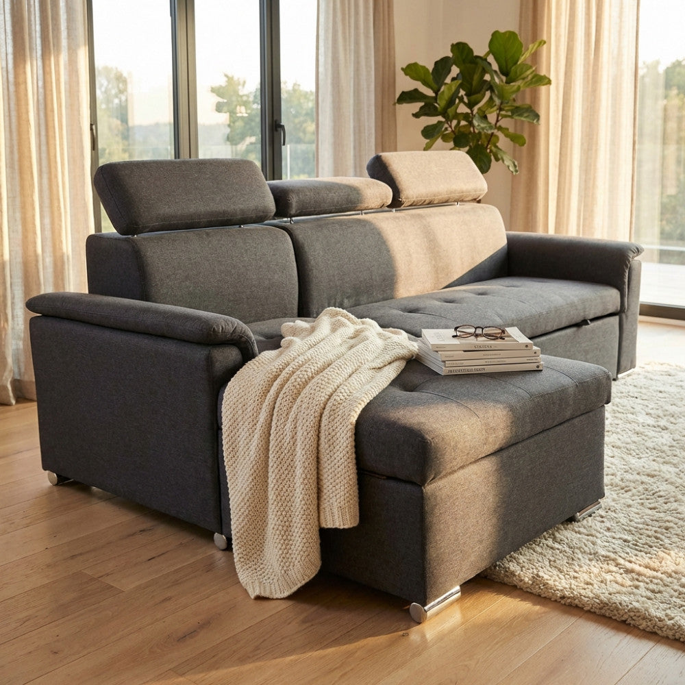 Soggiorno luminoso con divano Derrick grigio scuro, pouf contenitore, coperta in maglia e tavolino con libri.